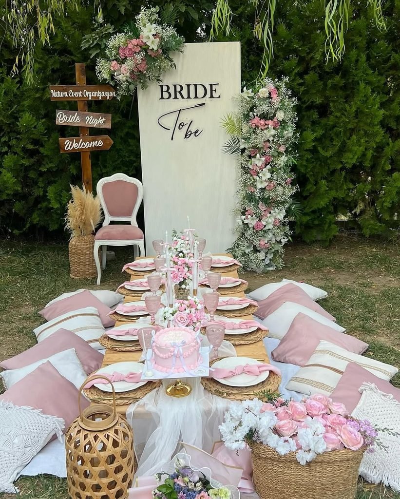 outdoor picnic style bridal shower with pink pillows and floral backdrop.