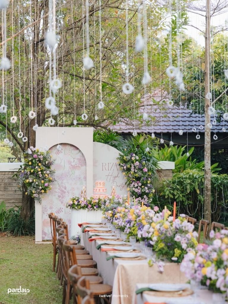 outdoor high tea party with long floral tablescape, pink tiered cake, and hanging decorations