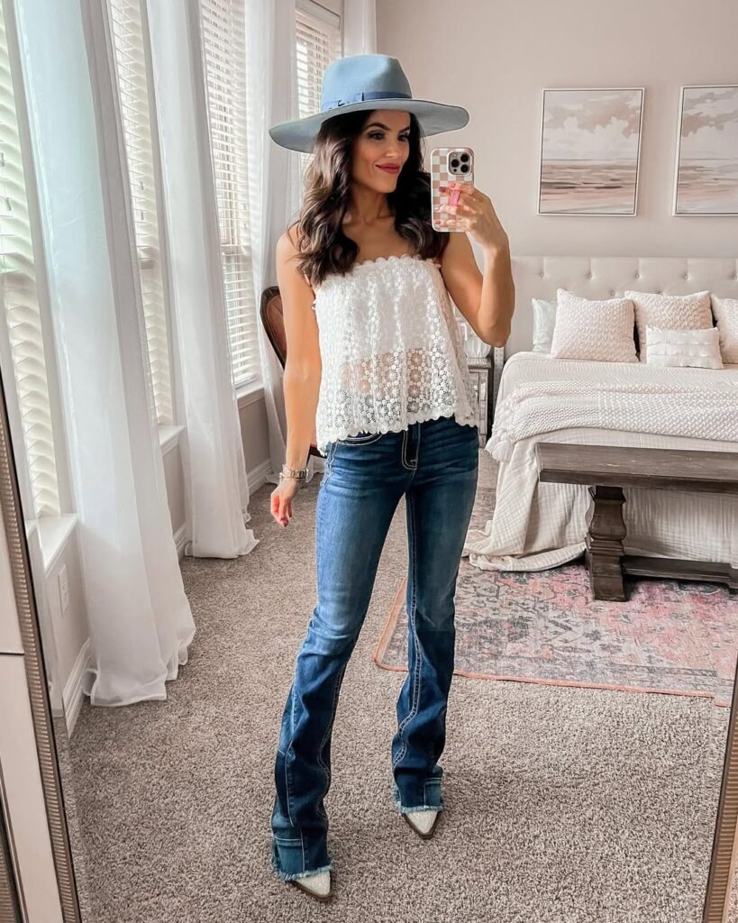 woman in a white lace top and flare jeans taking a mirror selfie indoors