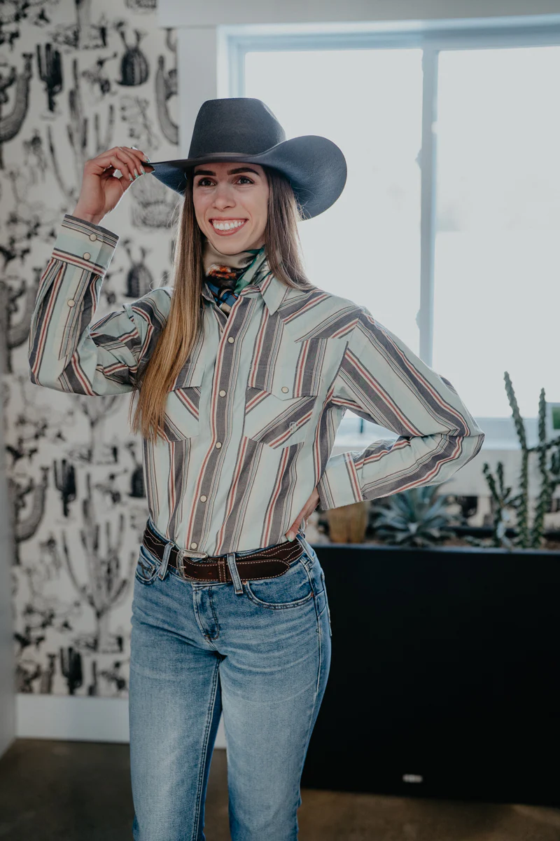 woman in a striped western shirt and cowboy hat posing against cactus print wallpaper