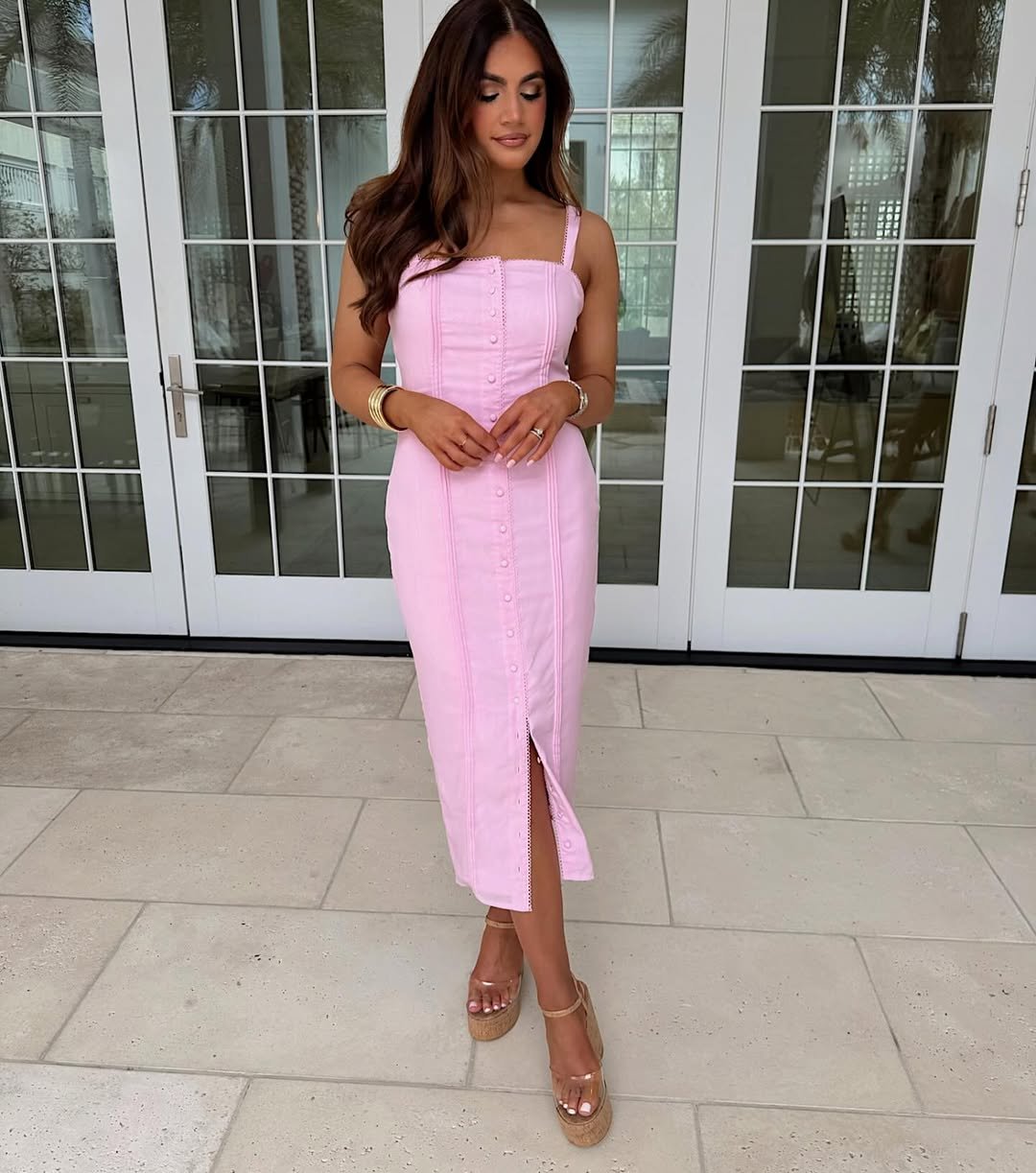 woman wearing a pink claire button down midi dress standing on a stone patio