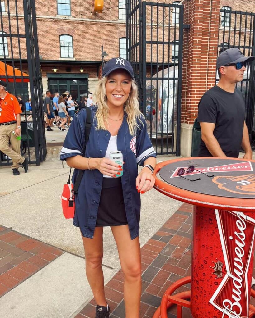 smiling woman in navy yankees jersey and black skort standing at stadium entrance