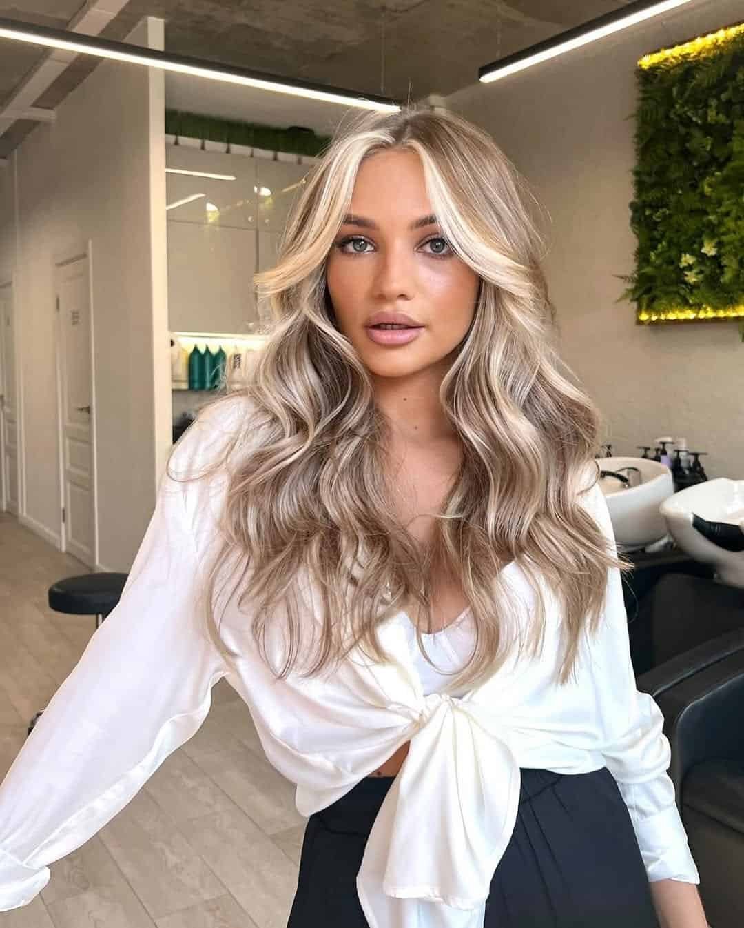woman with wavy blonde hair and bright face framing highlights in a salon