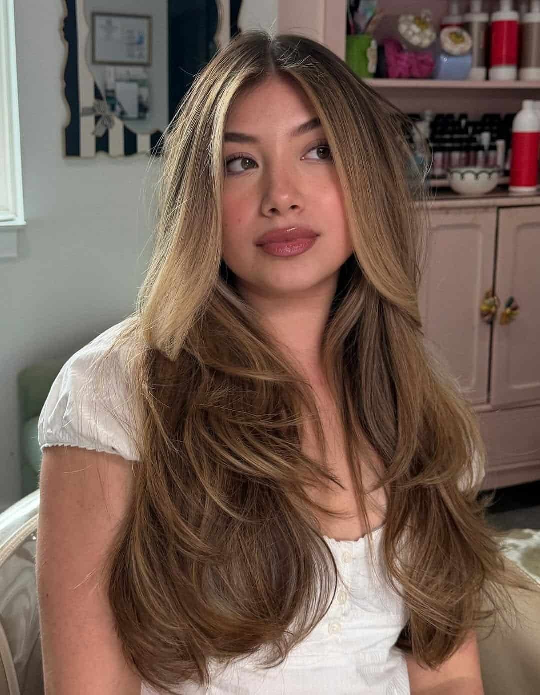 woman with long brunette layered hair and face framing blonde highlights