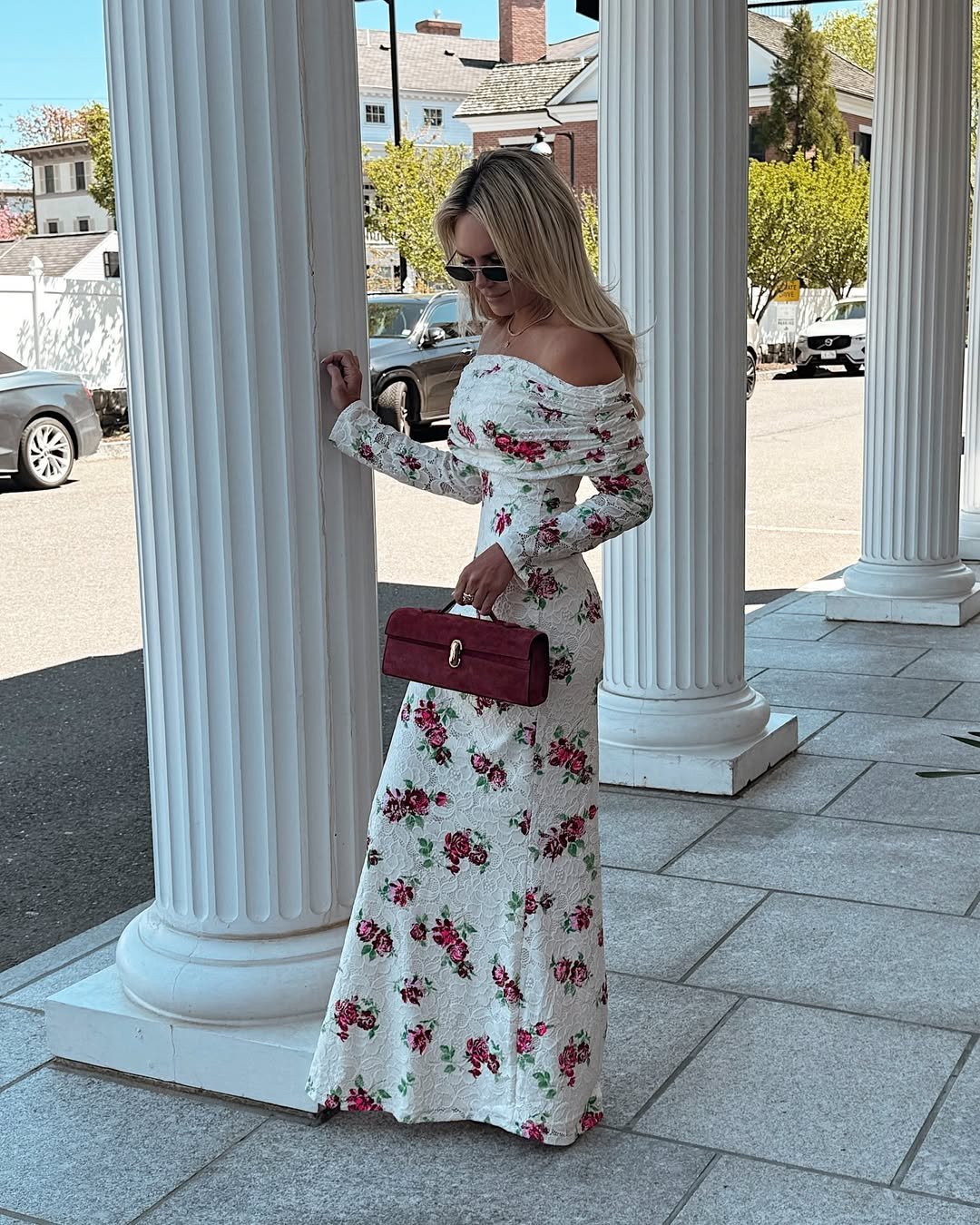 woman in a white floral off the shoulder maxi dress standing between white columns