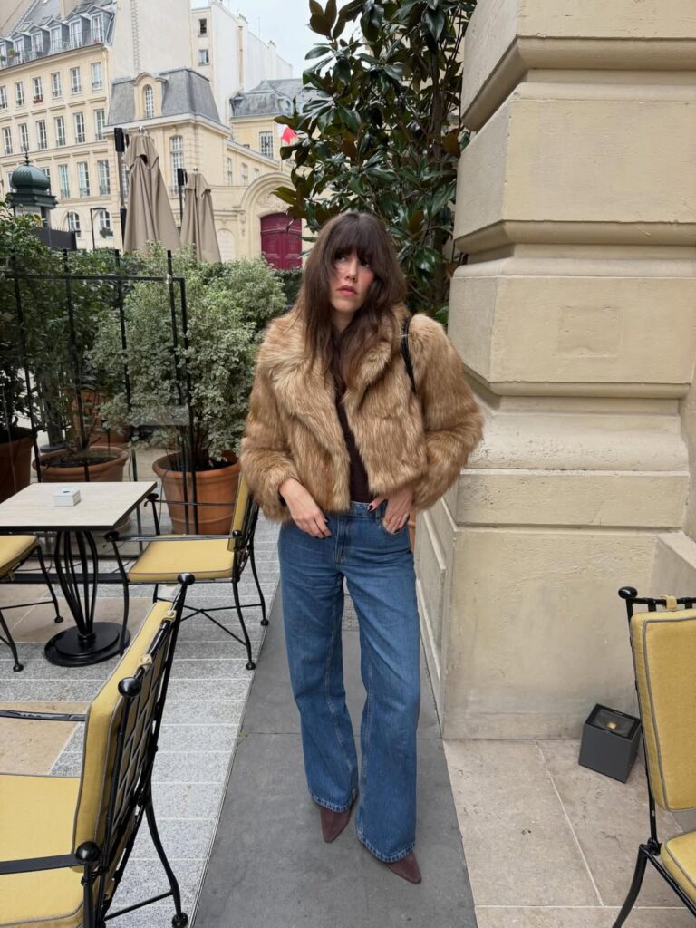 woman in a faux fur coat and blue jeans standing at a parisian cafe