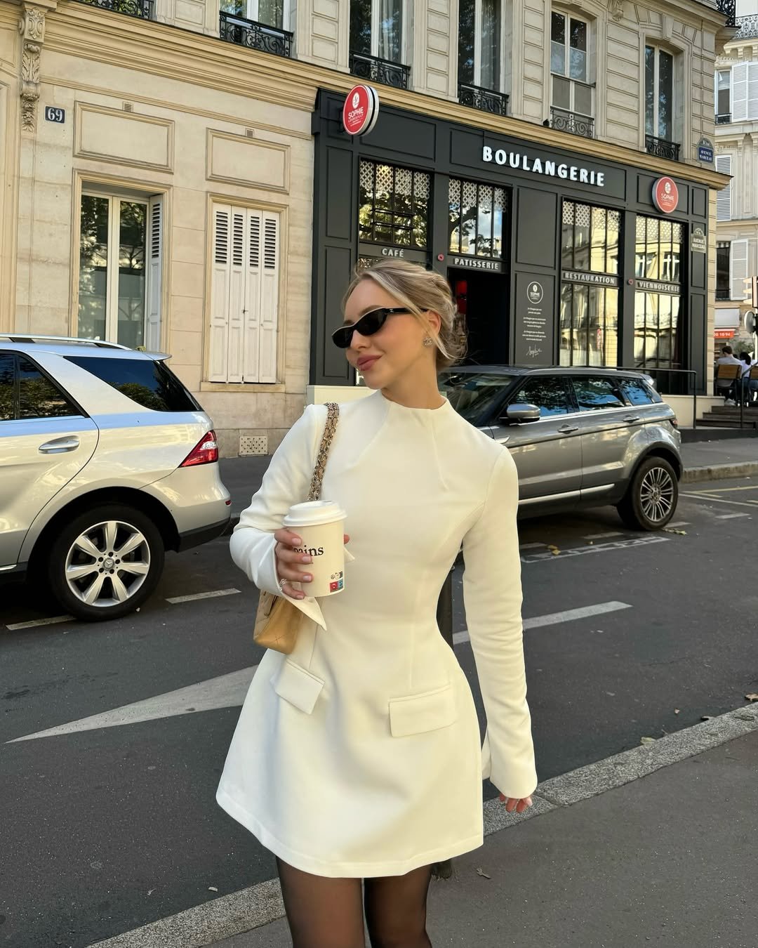 woman wearing a white long sleeve mini dress with pockets standing on a city street