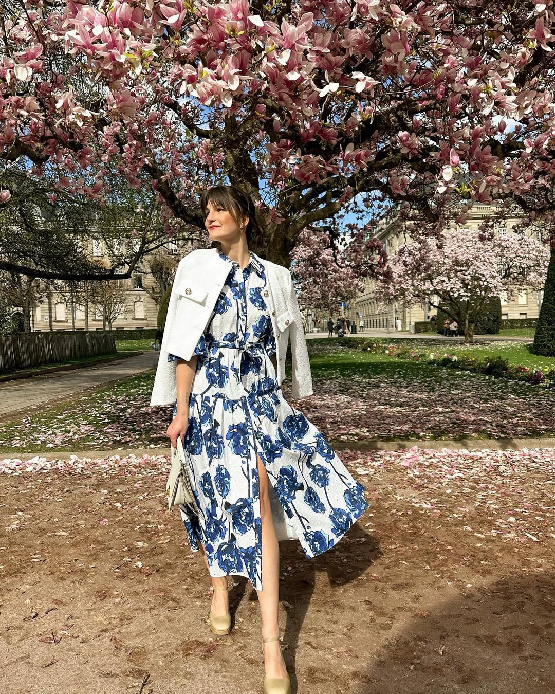 woman wearing a blue and white floral shirt dress under a blooming magnolia tree