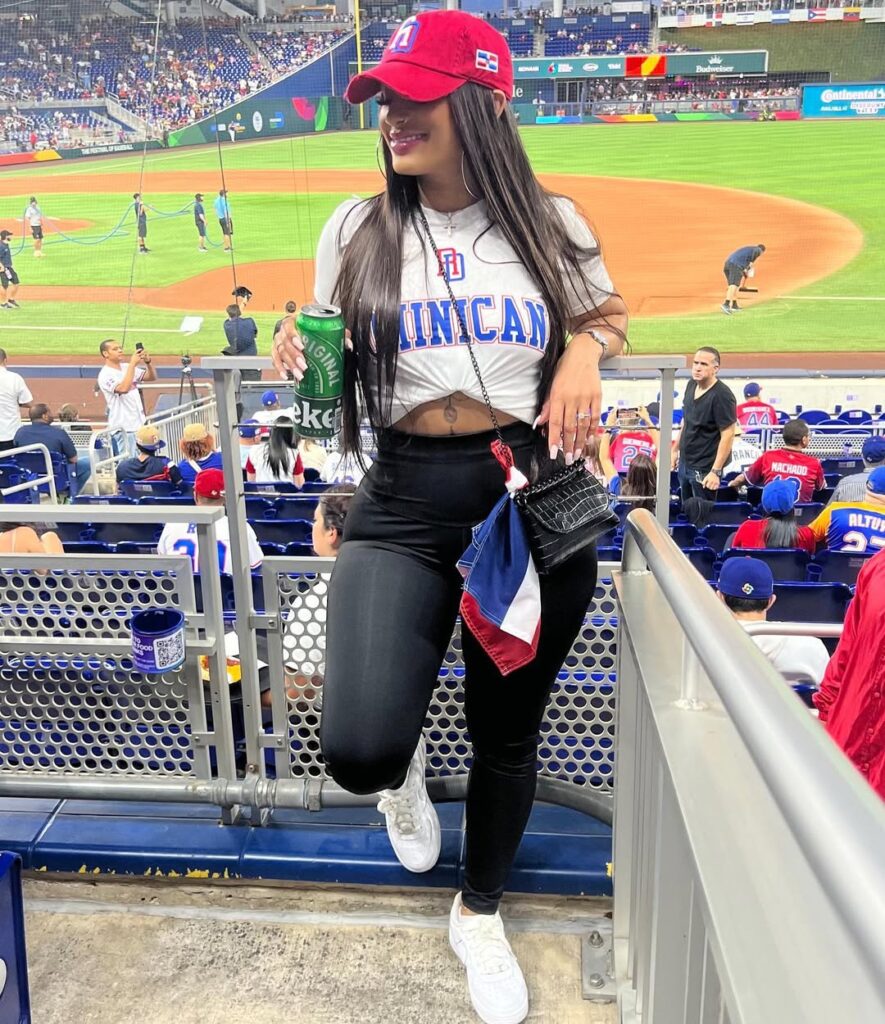 woman in dominican republic t-shirt and red hat holding drink at baseball game