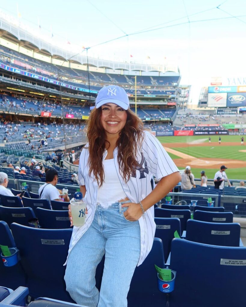 smiling woman wearing light blue yankees hat and pinstripe jersey at baseball stadium