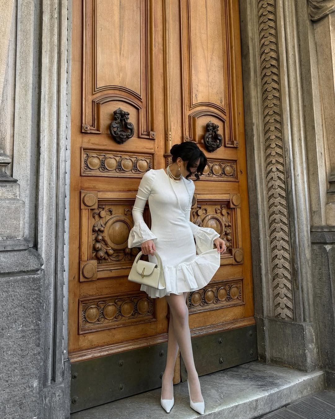 woman in a white ruffled mini dress posing in front of a carved wooden door