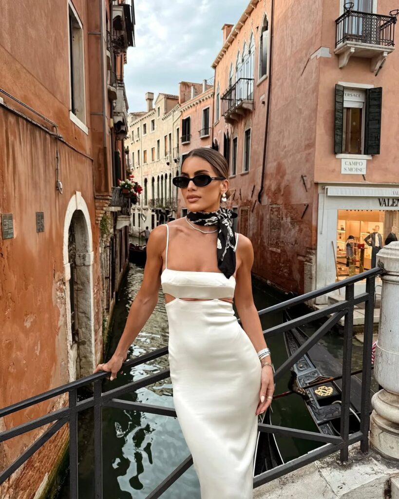 woman in white satin cutout dress with neck scarf standing on a venice bridge