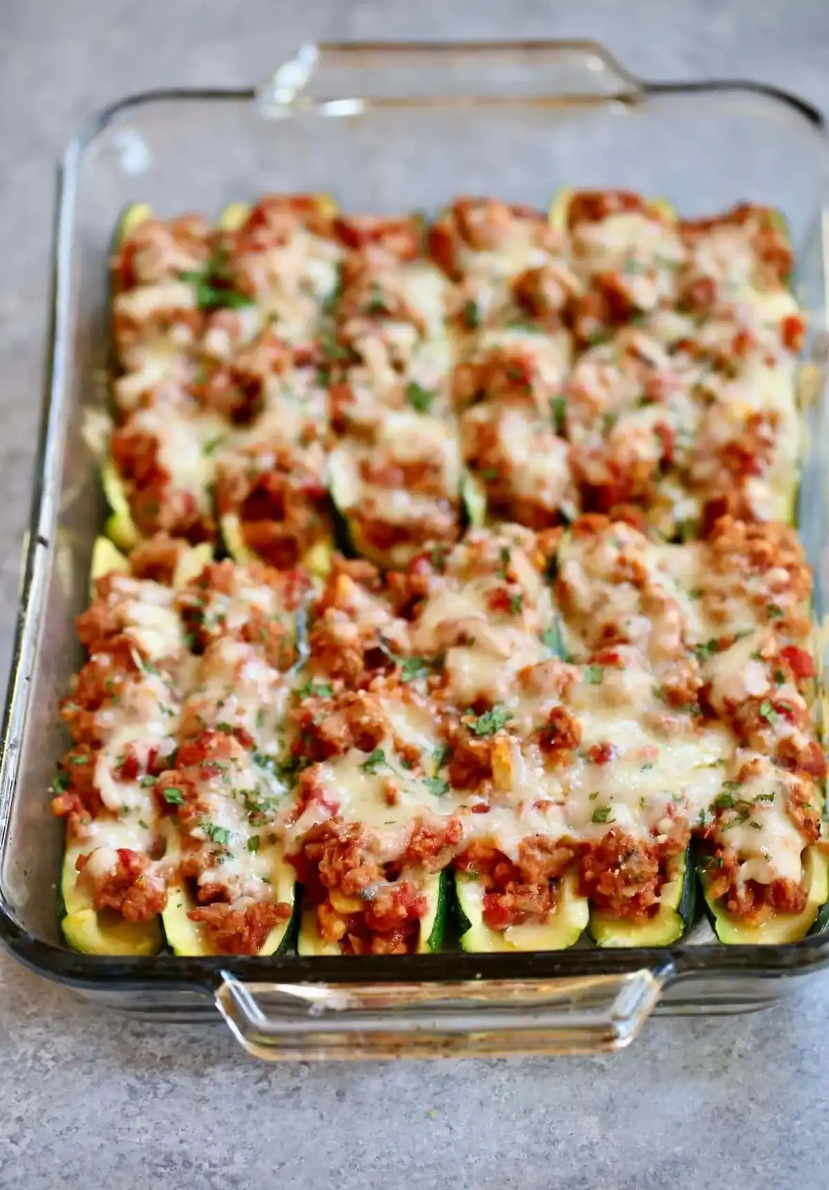 ground meat and tomato sauce stuffed zucchini boats topped with melted cheese in a glass dish.