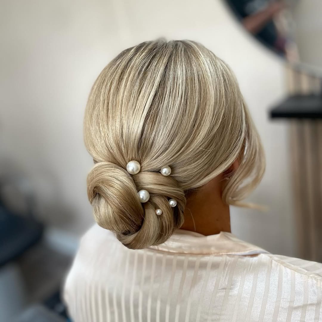blonde low bun hairstyle decorated with white pearls for a wedding
