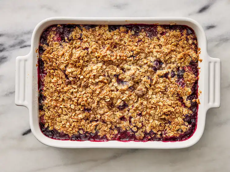 a golden brown mixed berry crisp with an oat topping in a white baking dish
