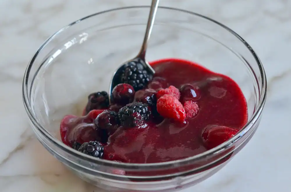 a glass bowl of thick red berry sauce mixed with whole blackberries and raspberries