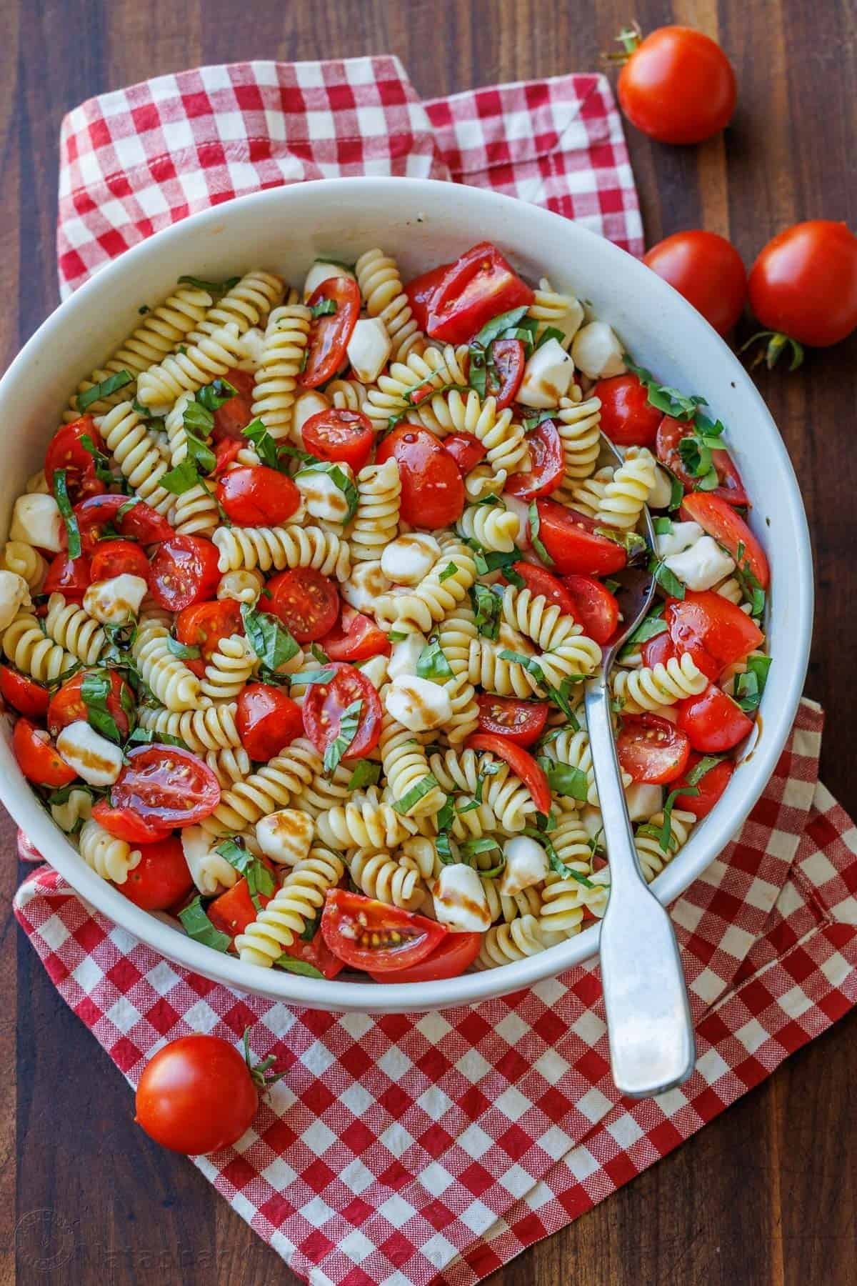 fusilli pasta salad with halved cherry tomatoes, fresh mozzarella pearls, and basil leaves.
