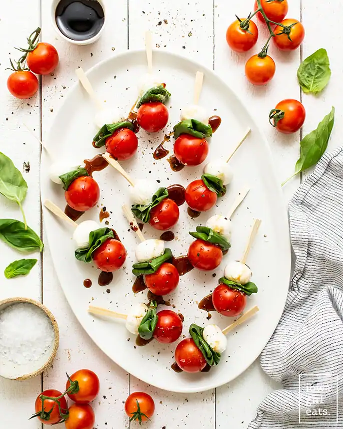 caprese skewers with cherry tomatoes, mozzarella, basil, and balsamic glaze drizzle