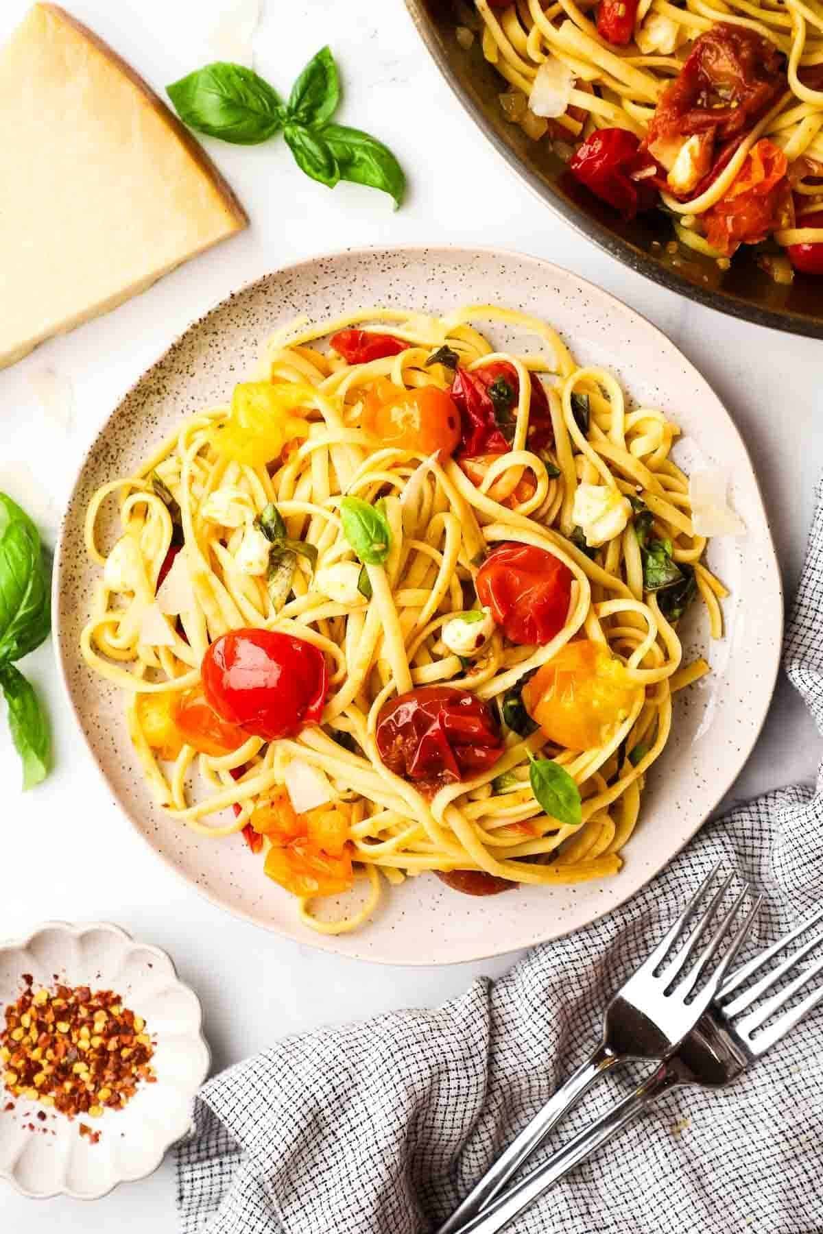 linguine pasta with burst cherry tomatoes, fresh basil leaves, and melted mozzarella on a plate.