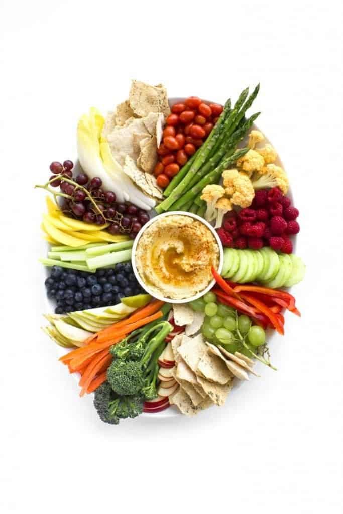 colorful vegetable and fruit crudite platter with hummus dip in the center
