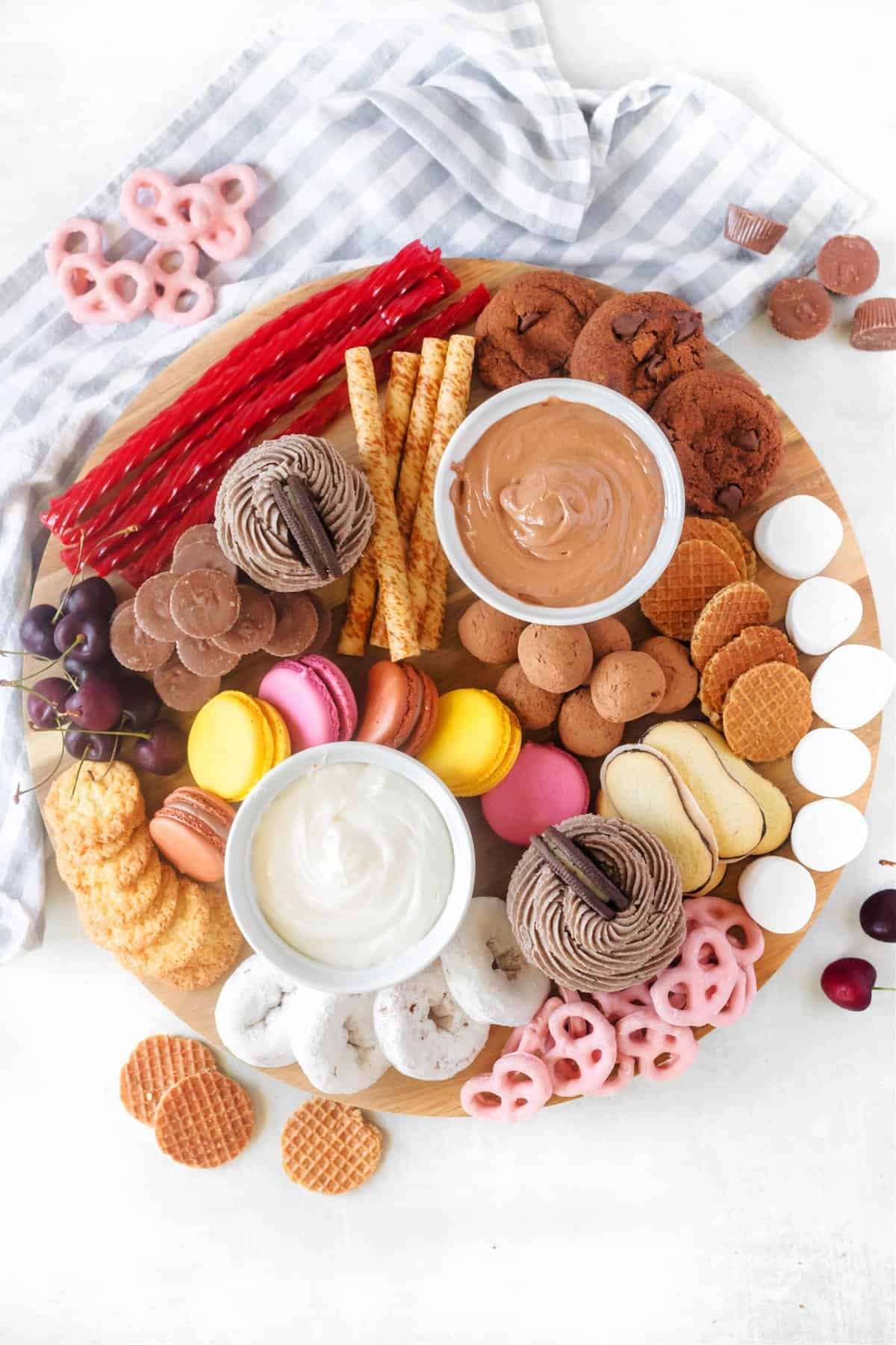 a large dessert charcuterie board with cookies, macarons, pretzels, dipping sauces, and fresh fruit