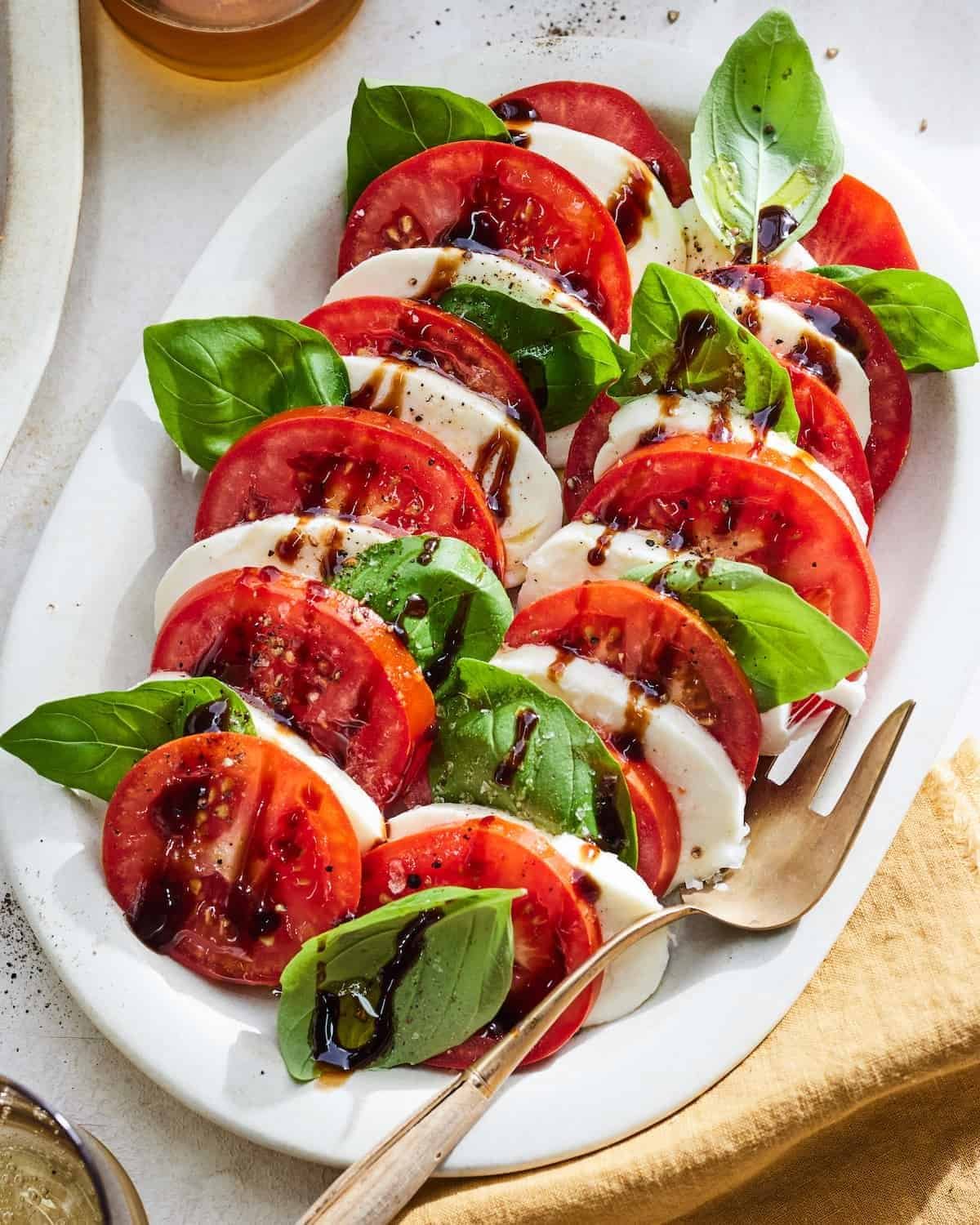 caprese salad with sliced tomatoes, mozzarella, basil leaves, and a balsamic glaze on a platter.