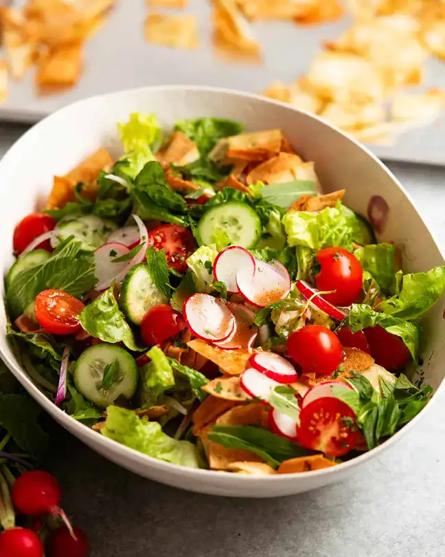 fattoush salad with crunchy pita chips, tomatoes, cucumbers, and radishes in a bowl.