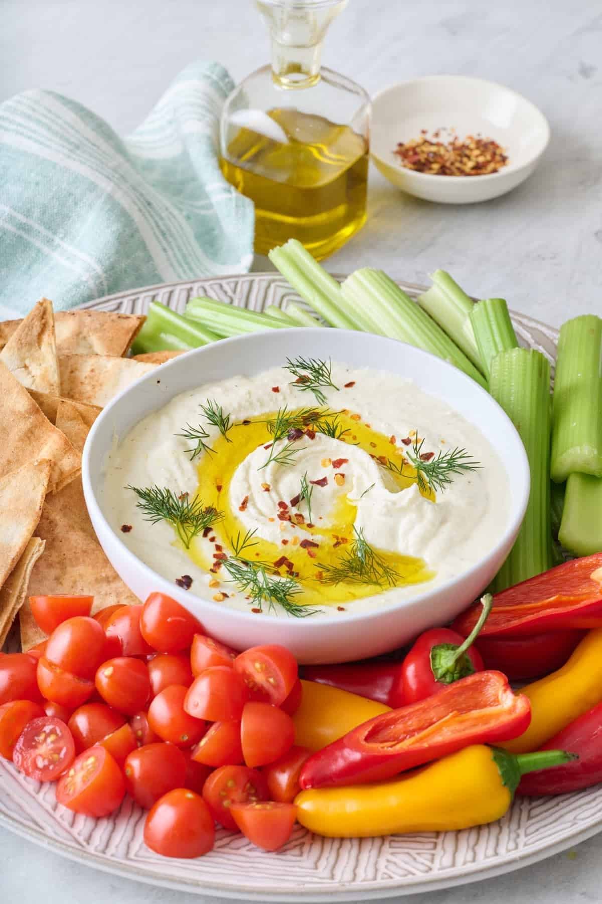 creamy feta dip garnished with herbs and olive oil beside fresh vegetables