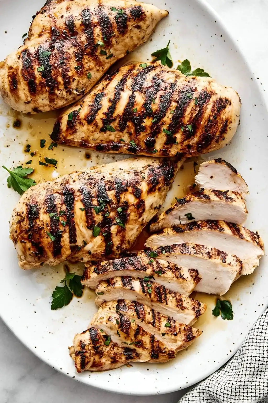 grilled chicken breasts with dark char marks and fresh parsley on a white serving platter.