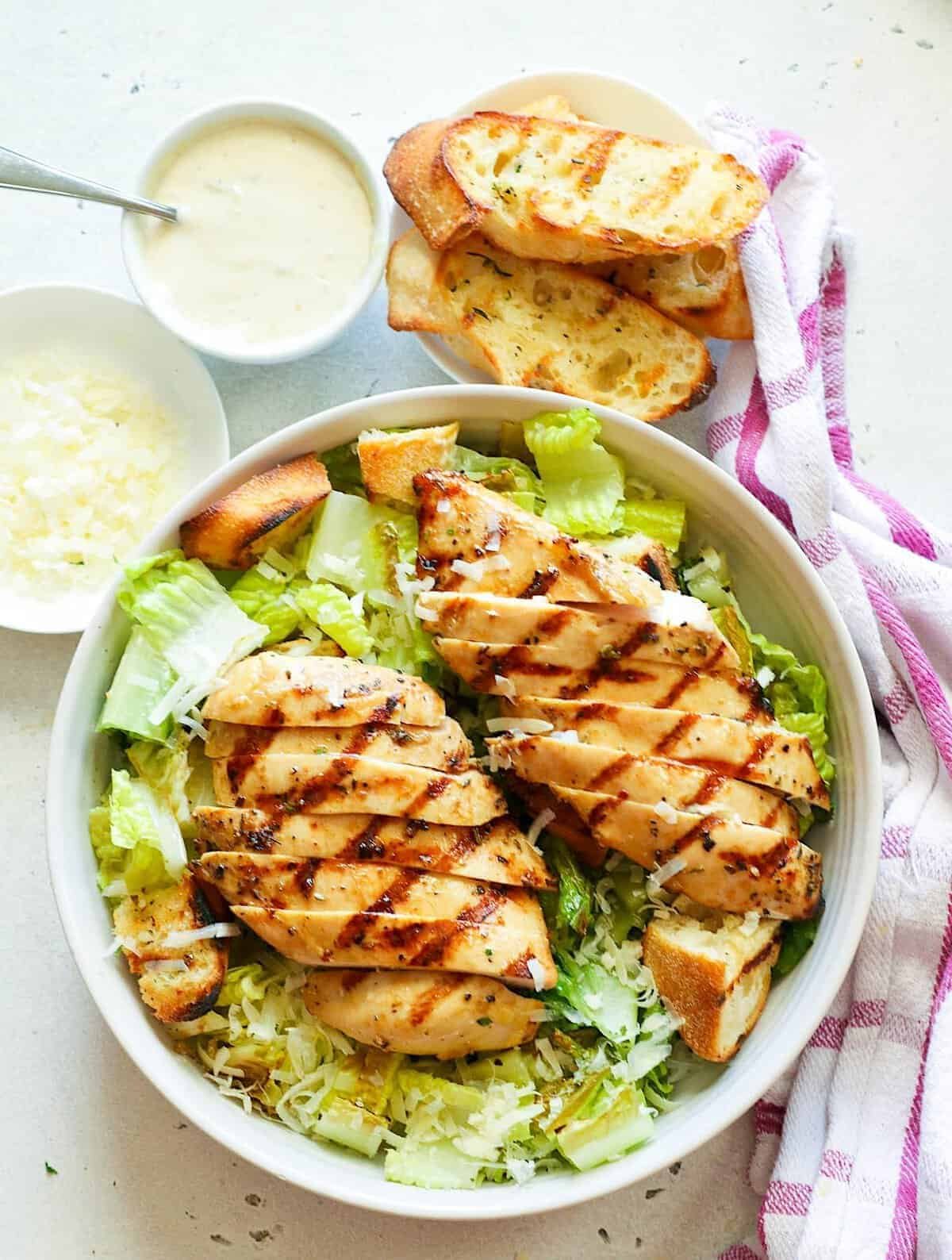 grilled chicken caesar salad with romaine lettuce, parmesan cheese, and toasted baguette slices.