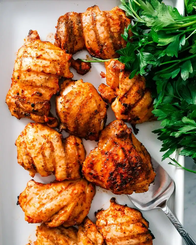 grilled chicken thighs with charred grill marks served on a platter with fresh parsley.