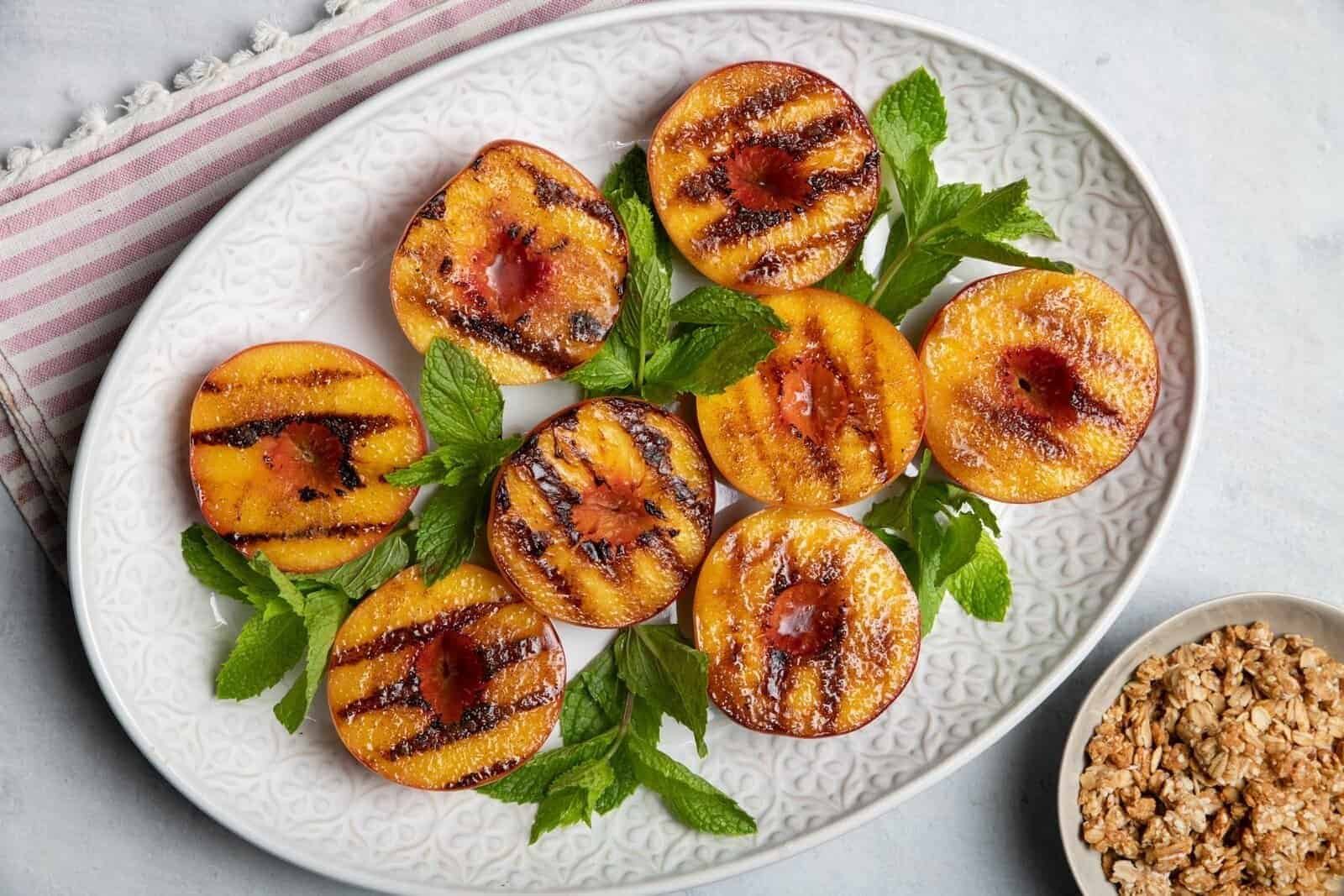 grilled peach halves with dark char marks served on a white platter with mint