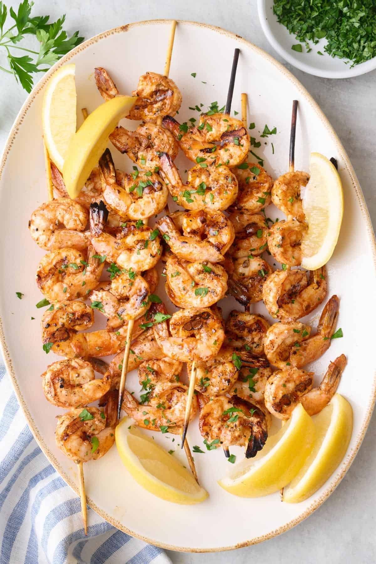 grilled shrimp skewers on a platter served with lemon wedges and fresh herbs.