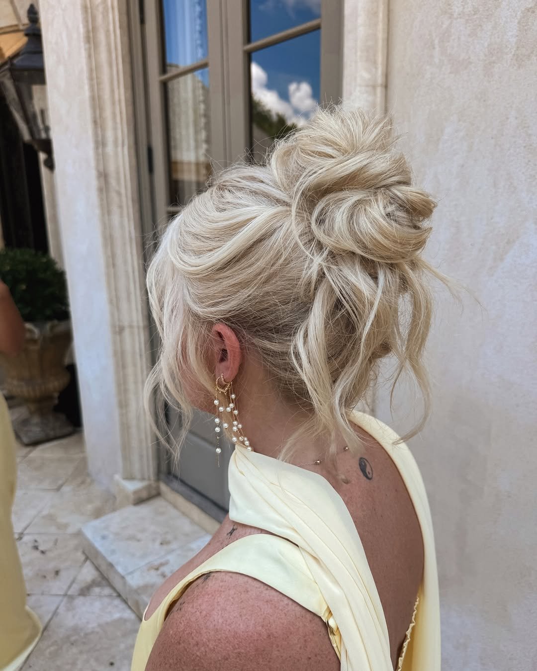 messy blonde bridal updo hairstyle with loose strands and pearl earrings