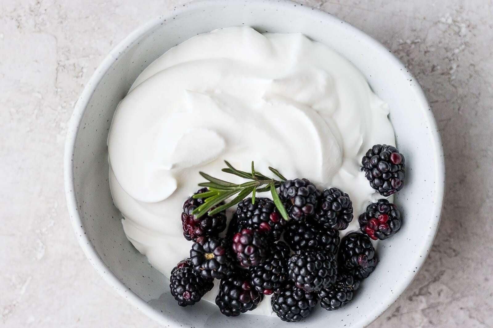 a bowl of fluffy homemade whipped cream topped with fresh blackberries and a rosemary sprig