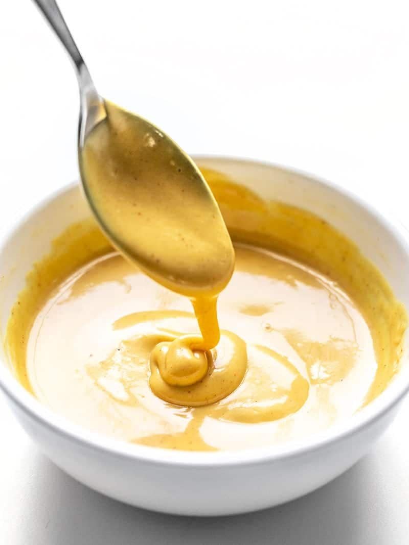 creamy honey mustard sauce dripping from a metal spoon into a white bowl