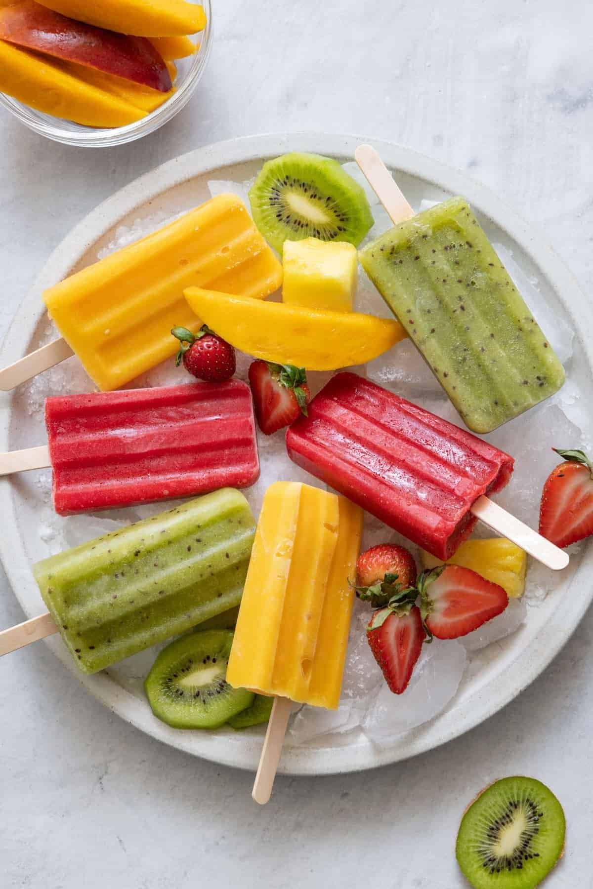 various fruit popsicles and fresh fruit slices arranged on a plate of crushed ice