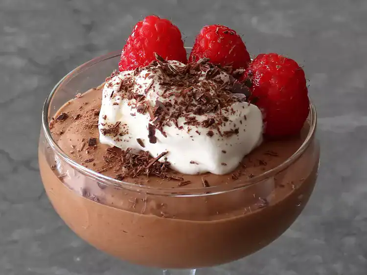 chocolate mousse in a glass bowl topped with whipped cream, chocolate shavings, and raspberries