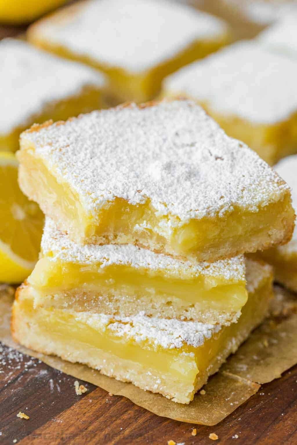 a stack of three zesty lemon bars with a thick crust and powdered sugar coating