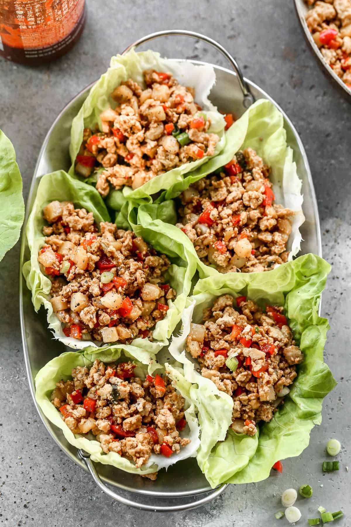 savory ground chicken and vegetable filling served in fresh green lettuce wraps on a metal tray.