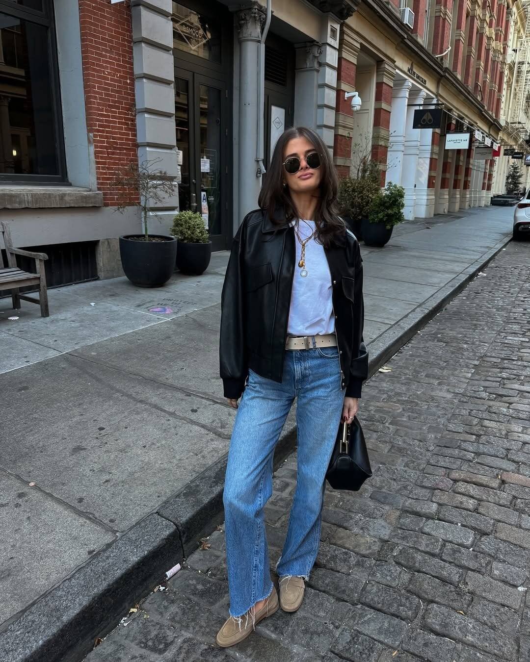 woman in black leather jacket and blue jeans standing on a cobblestone street