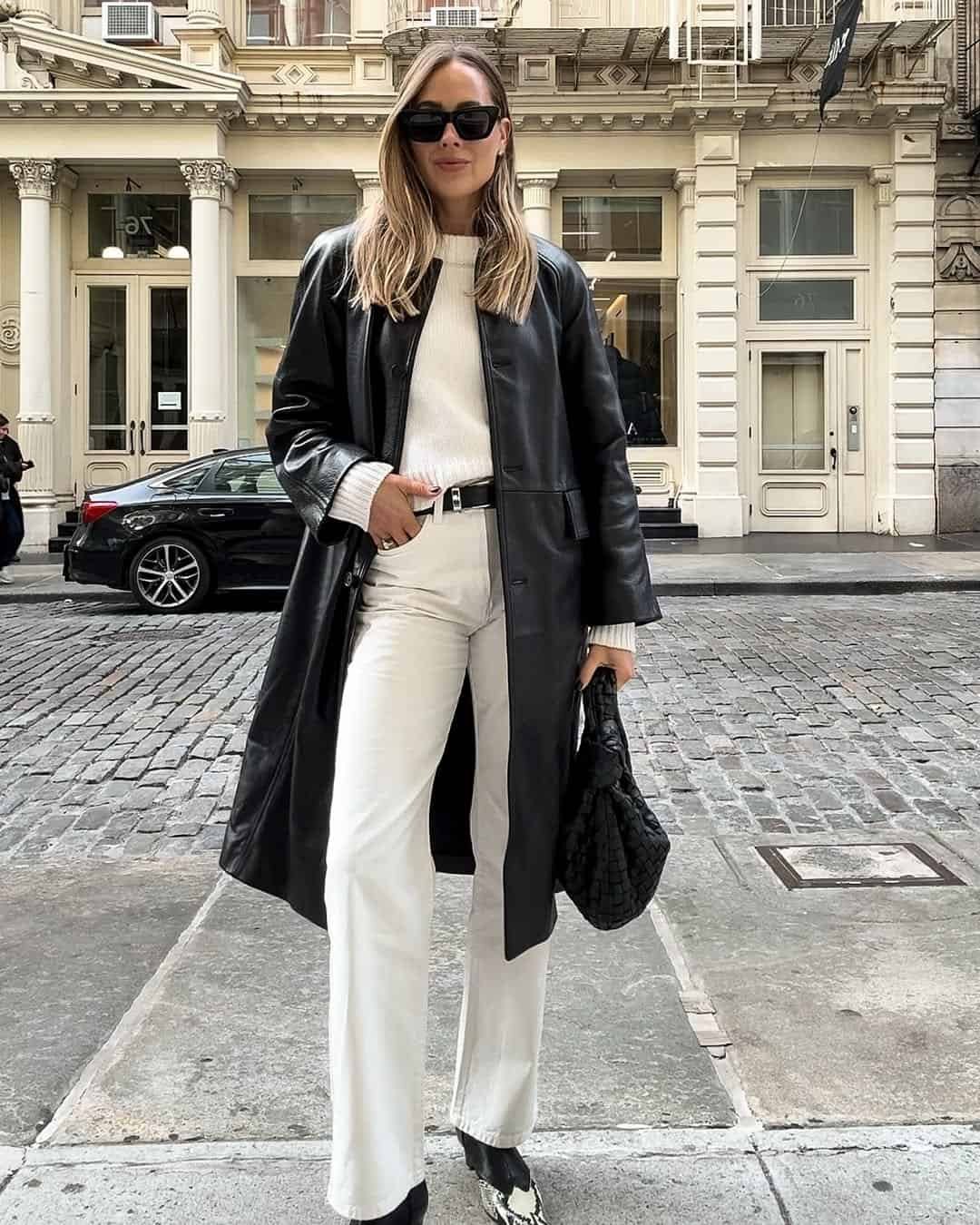 woman in long black leather coat and white trousers on a cobblestone street