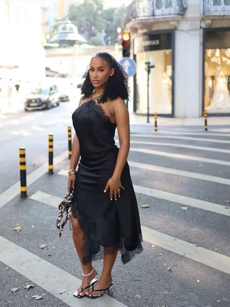 woman in black lace slip dress and strappy sandals standing on a crosswalk