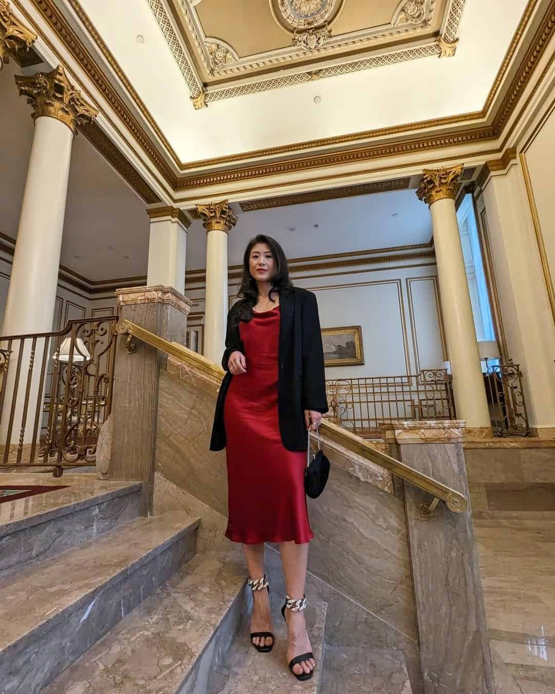woman in red silk slip dress and black blazer standing on marble stairs