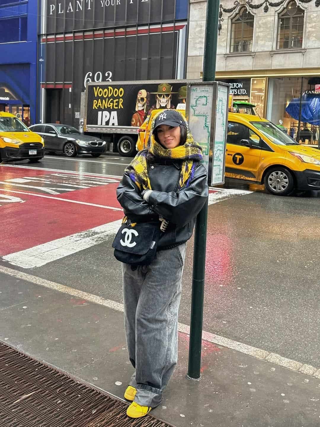 woman in black leather jacket and yellow scarf leaning against a green pole
