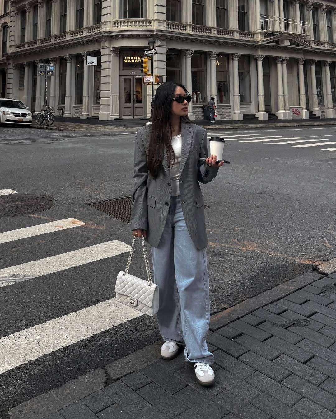 woman in grey oversized blazer and baggy jeans carrying a white quilted handbag