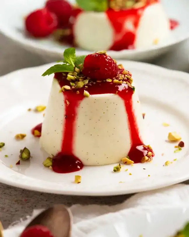 vanilla panna cotta with raspberry sauce, fresh raspberries, and crushed pistachios on a plate