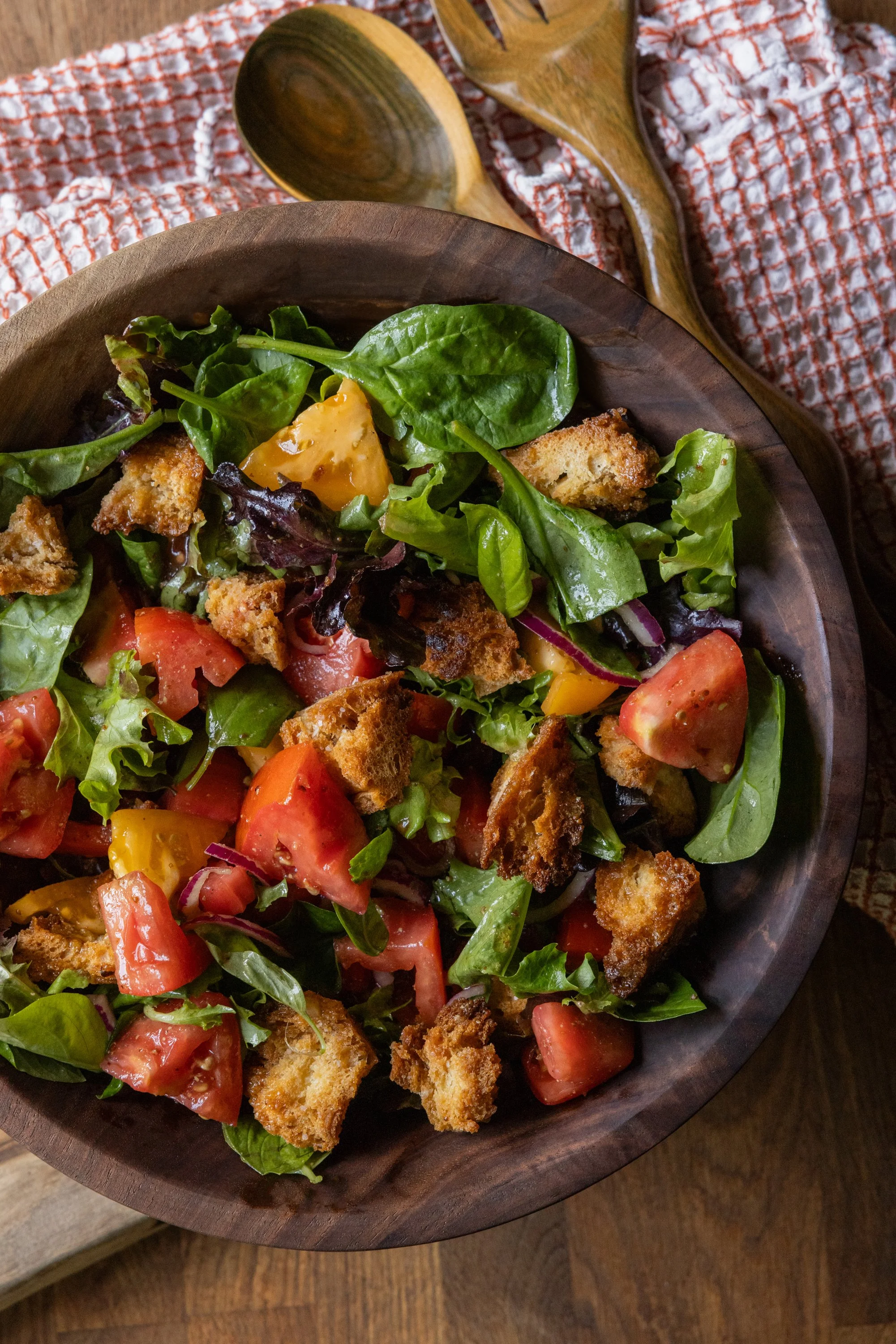 panzanella salad with toasted bread cubes, tomatoes, and leafy greens in a wooden bowl.