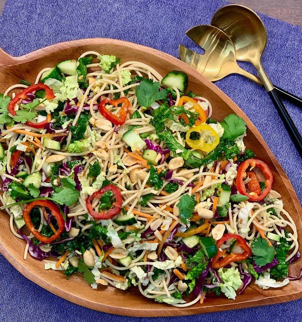 sesame ginger noodle salad with peppers, peanuts, and herbs in a wooden bowl.
