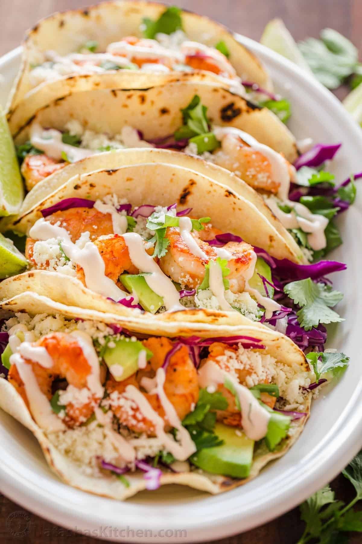 shrimp tacos with avocado, purple cabbage slaw, and creamy sauce in charred flour tortillas.